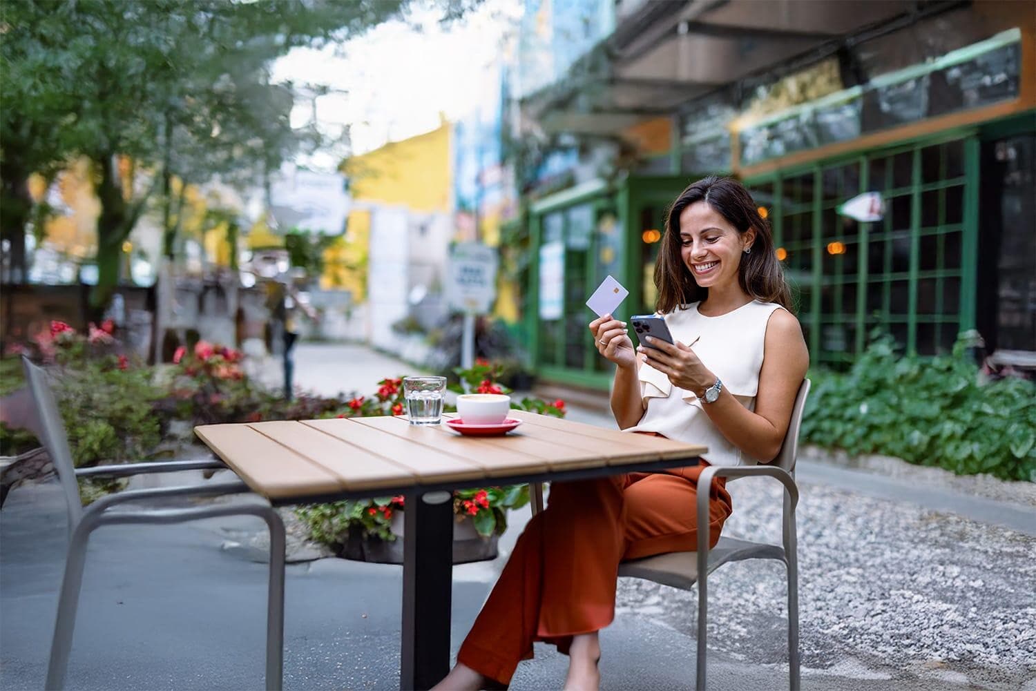 Woman at outdoor cafe on smartphone with credit card